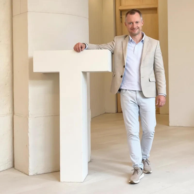 Matthias Völker, Strategie & Wissensmanagement bei SaPeReS, neben dem monumentalen Buchstaben T – Teil der KI-TEAM-Bildserie von Sanne Jerxsen